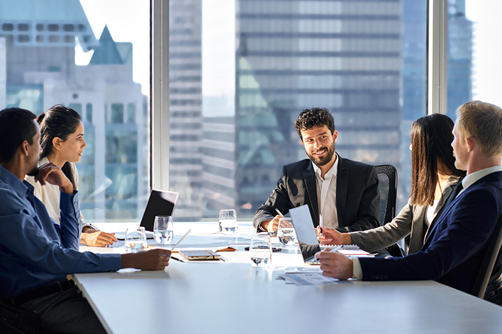 Photo de 5 hommes et femmes d'affaire autour d'un bureau discutant business dans une salle de réunion