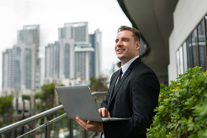 Photo d'un homme d'affaires en costume tenant son ordinateur sur un balcon extérieur