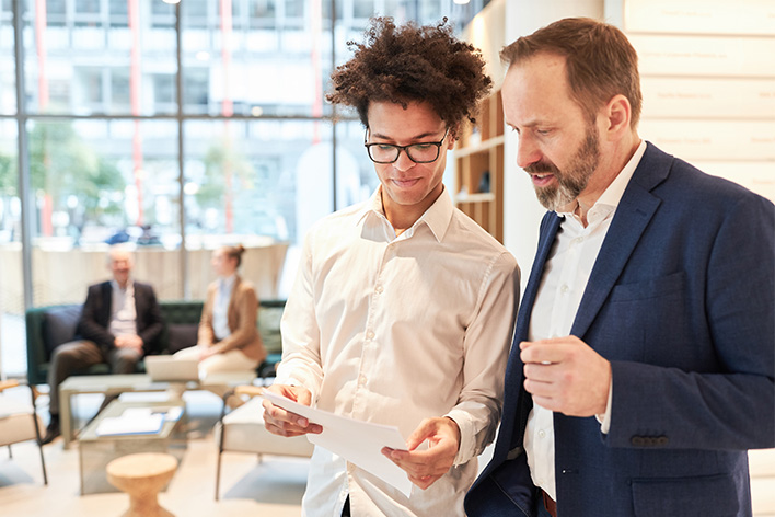 Photo de deux hommes en train de parler business avec des documents en main dans un hall